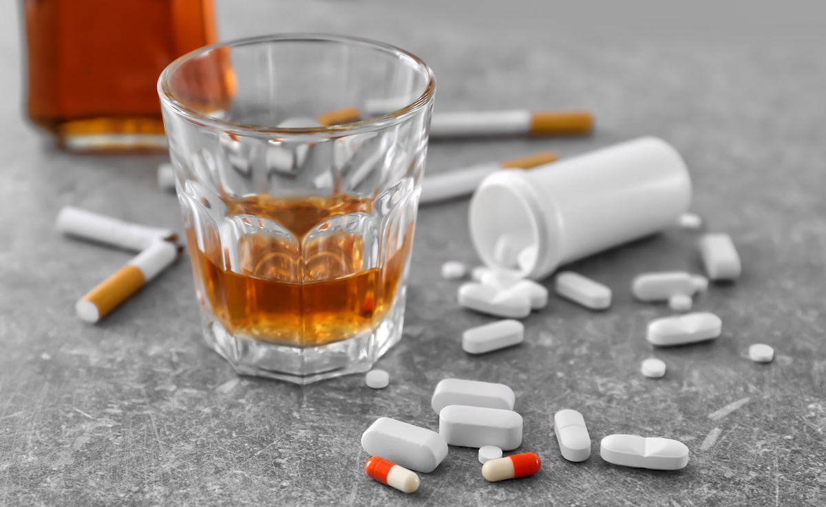 Glass of alcohol, cigarettes and drugs on table.