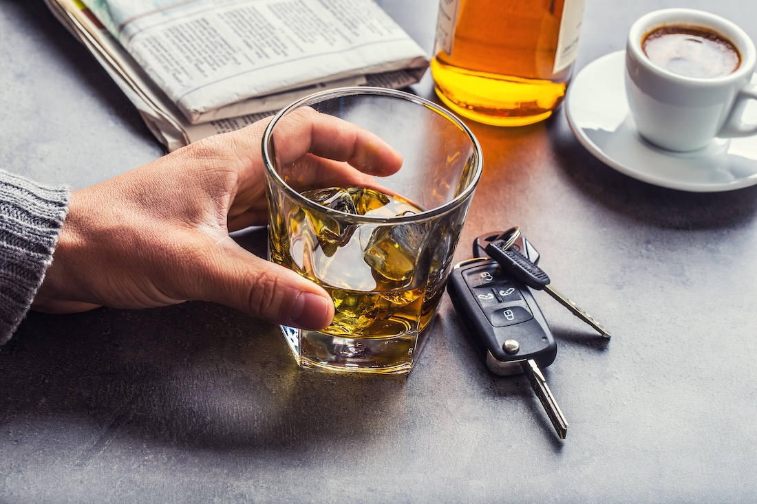 Man's hand holding a glass of alcohol next to car keys