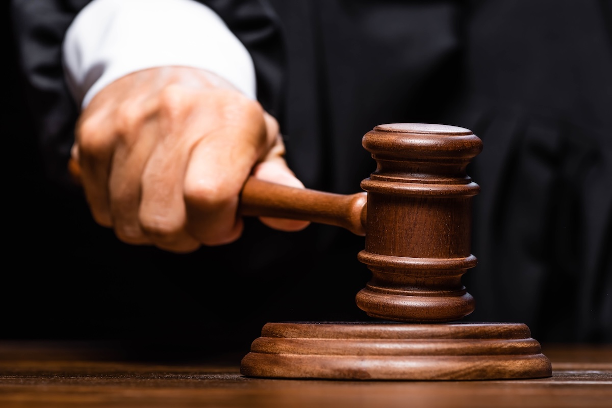 cropped view of judge in judicial robe sitting at table and hitting with gavel