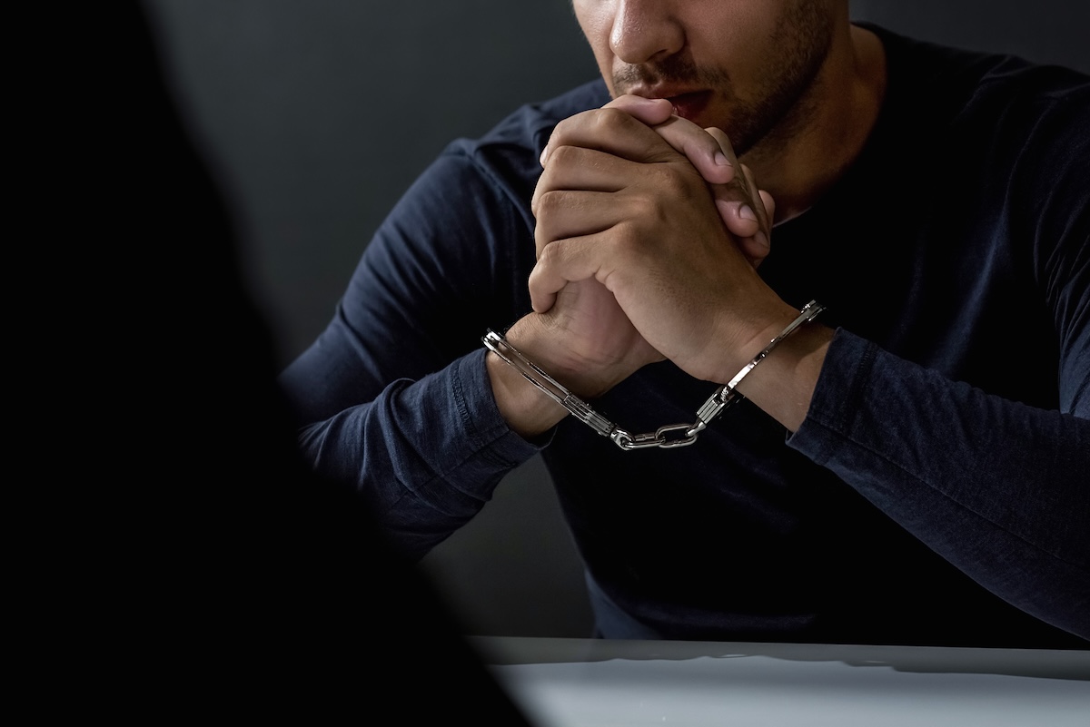 Criminal man with handcuffs in interrogation room feeling guilty after being arrested a crime