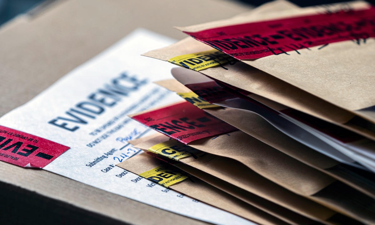 A stack of brown evidence envelopes with red and yellow evidence tape sits on top of an evidence submission form, suggesting items collected for a criminal investigation.