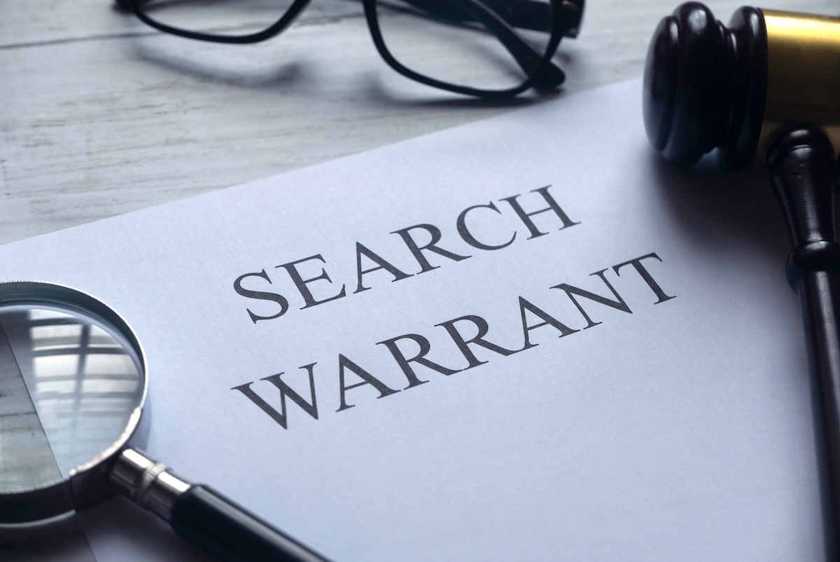 Selective focus of magnifying glass, gavel, glasses and paper written with Search Warrant on white wooden background.