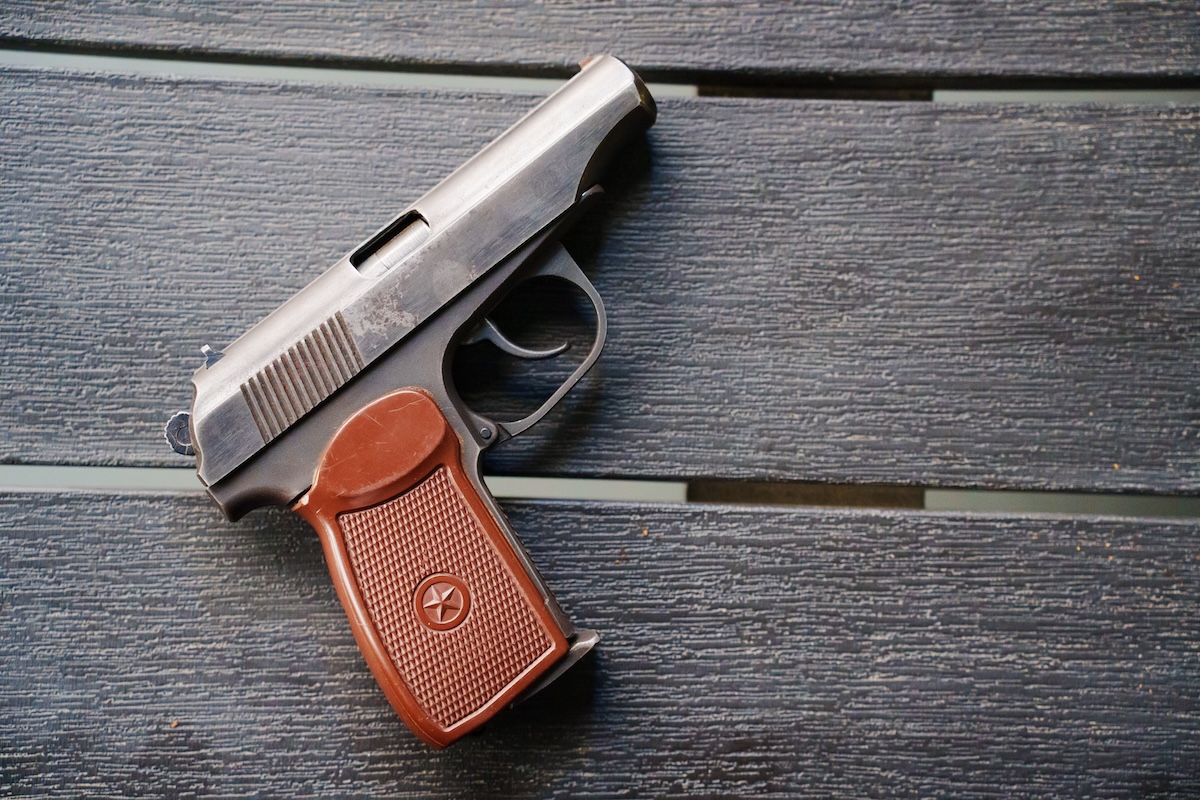 A small semi-automatic handgun with a brown textured grip and a star emblem, resting on a dark wooden surface.