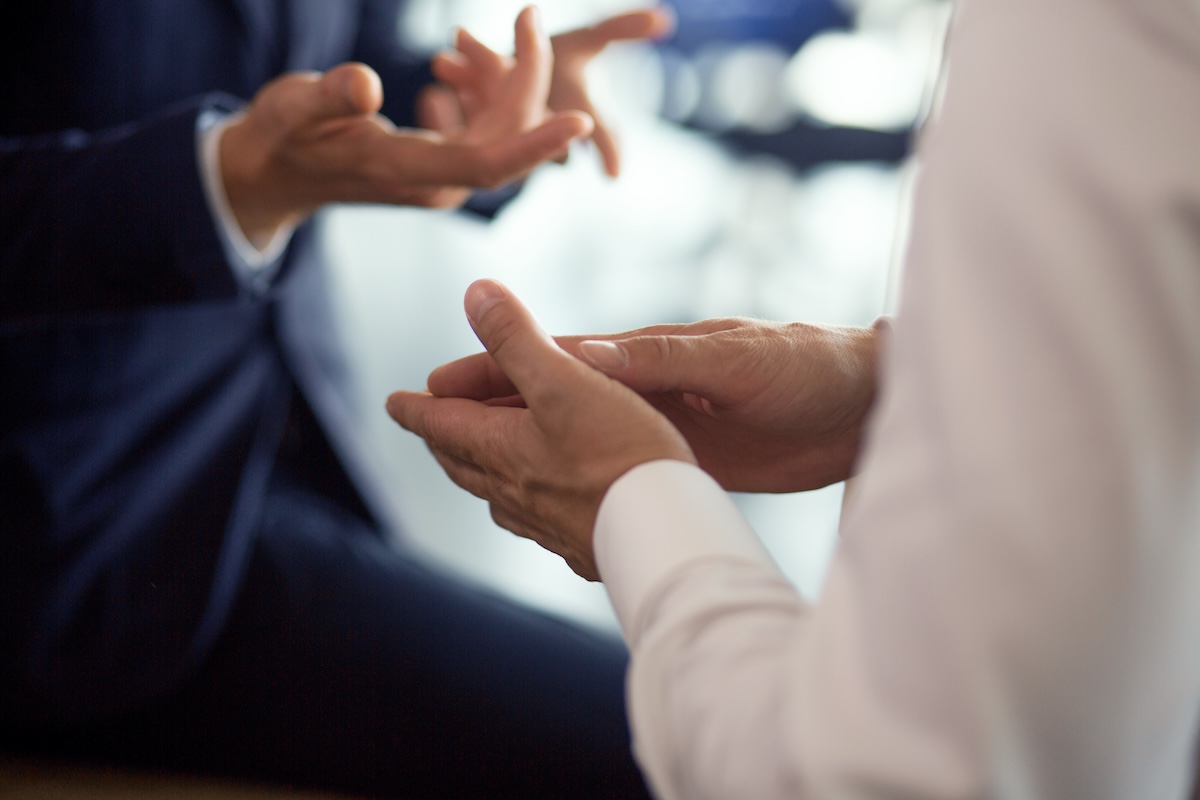 Close-up of two people in business attire having a conversation, with focus on their hands gesturing expressively. Their faces are not visible.