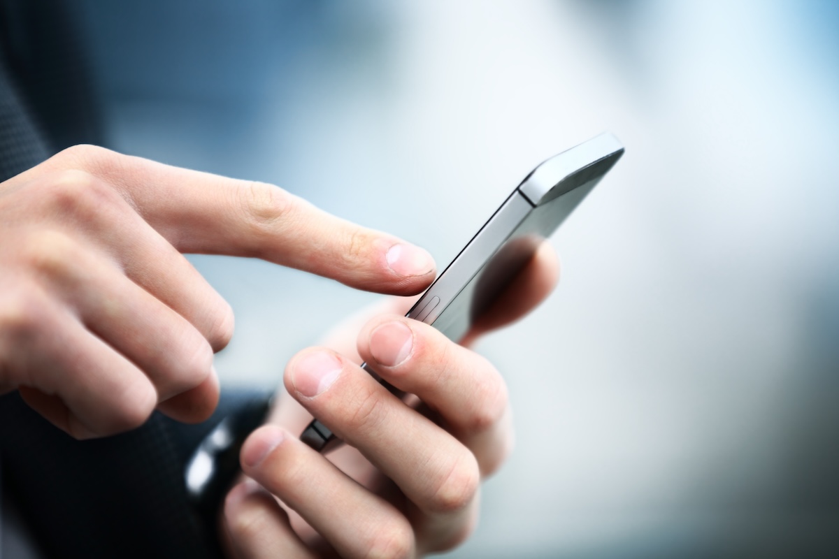 A close-up of a person’s hand holding a smartphone while using their index finger to touch the screen, with a blurred background.