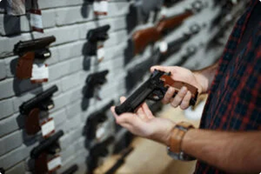 A person in a plaid shirt is holding a handgun in a store, with a display wall of various handguns mounted in the background.