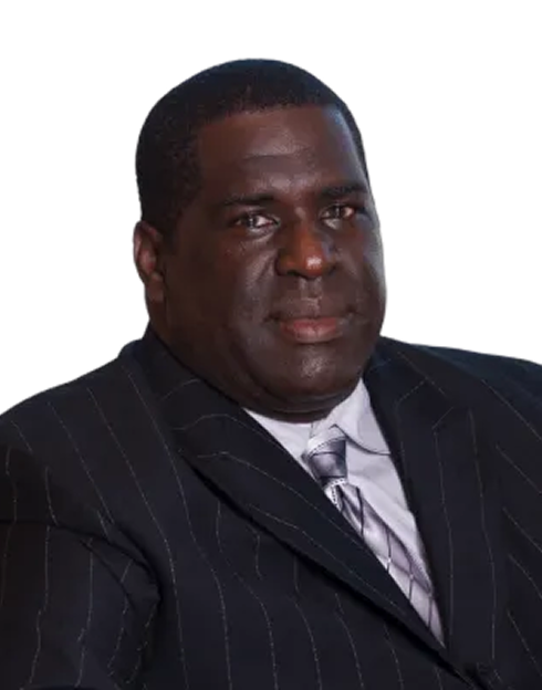 A man wearing a dark pinstripe suit, light-colored shirt, and patterned tie, looking at the camera with a neutral expression, against a plain white background.